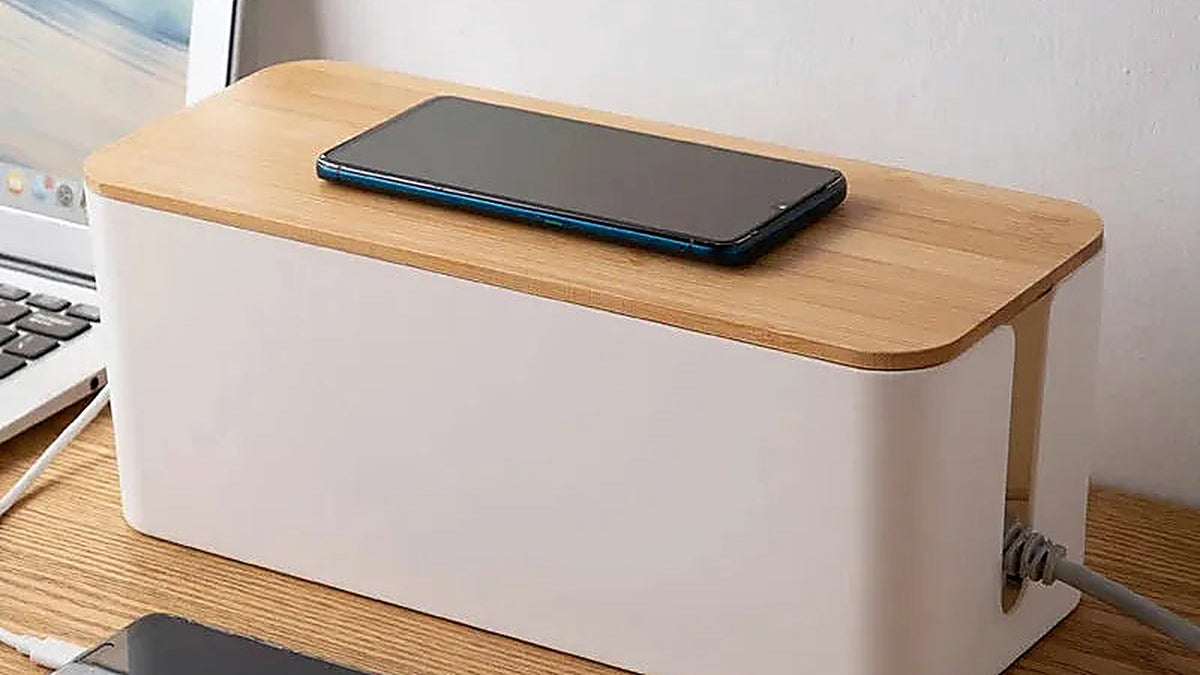 White cable management box with a bamboo lid on a wooden desk, charging a phone