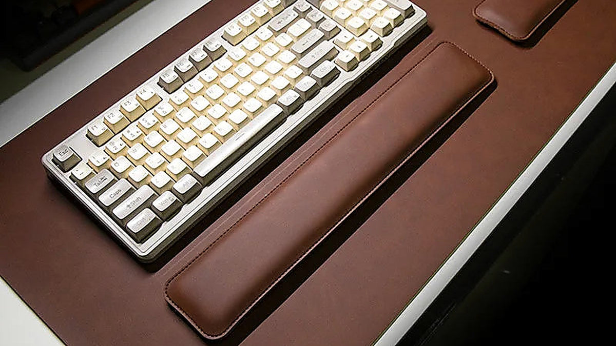 Brown leather desk mat with a cream mechanical keyboard and matching wrist rest