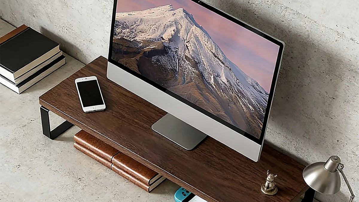 Walnut and steel monitor riser lifting an all-in-one screen on a desk against a concrete wall